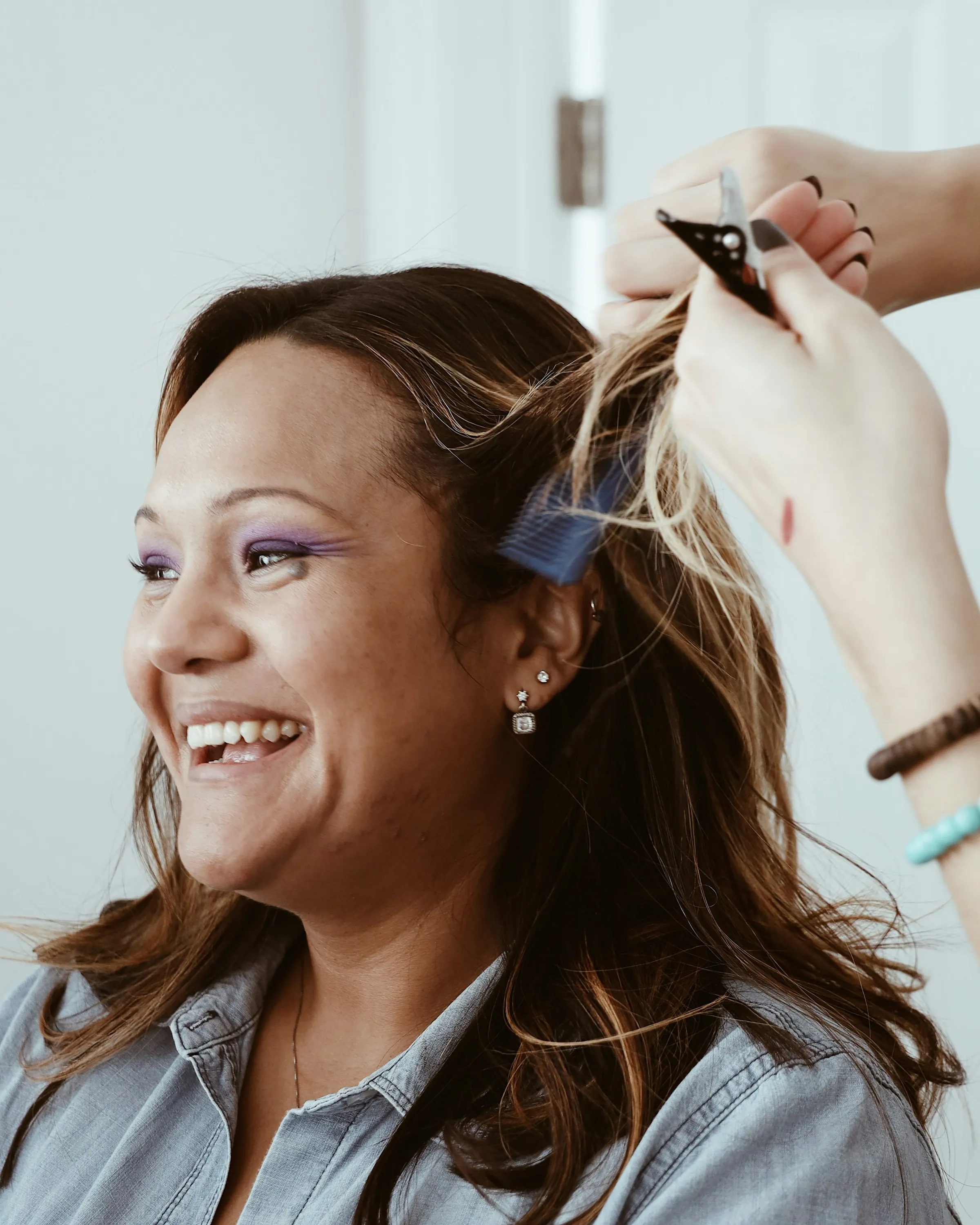 Scissors at work on dark brown hair while the client laughs