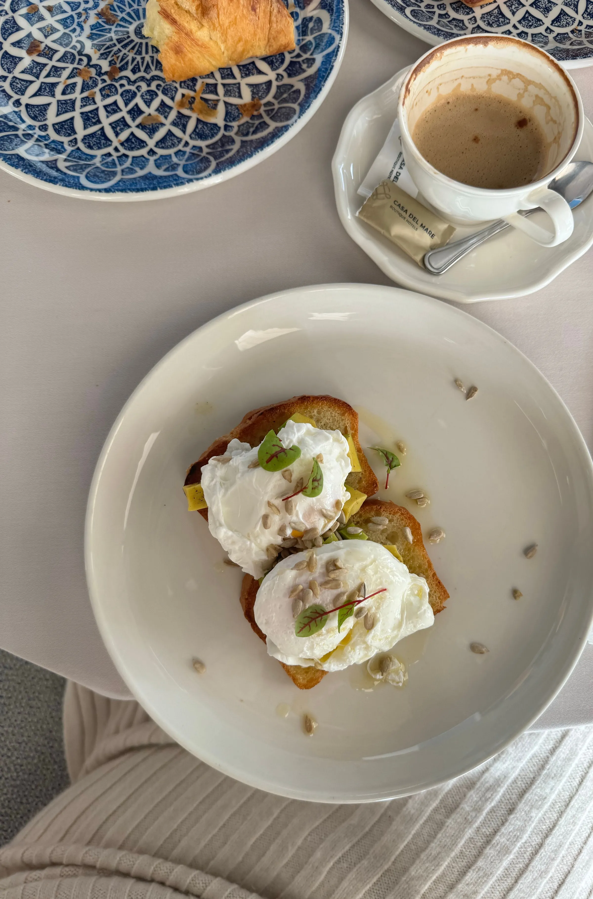 Poached eggs on toast on a white plate beside a cappuccino, seen from above