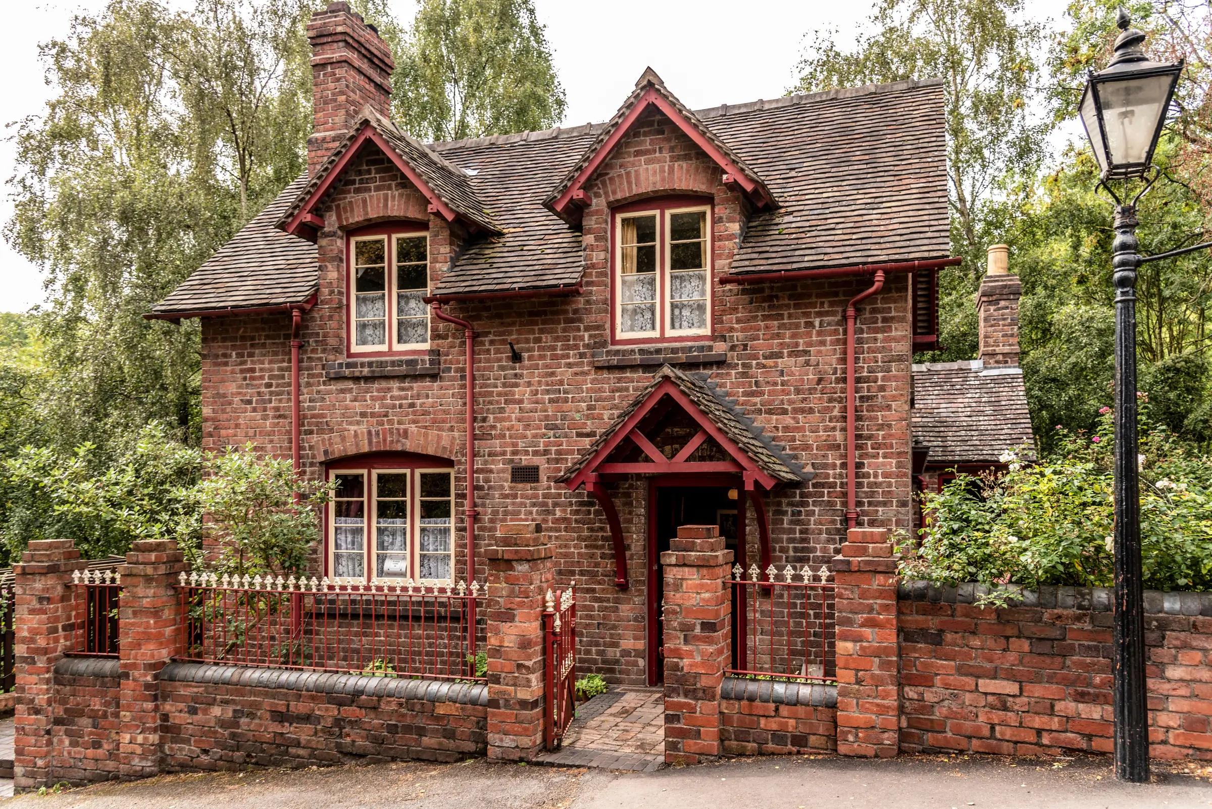 A red-brick cottage with tall chimneys, a low brick wall and a lamp post outside