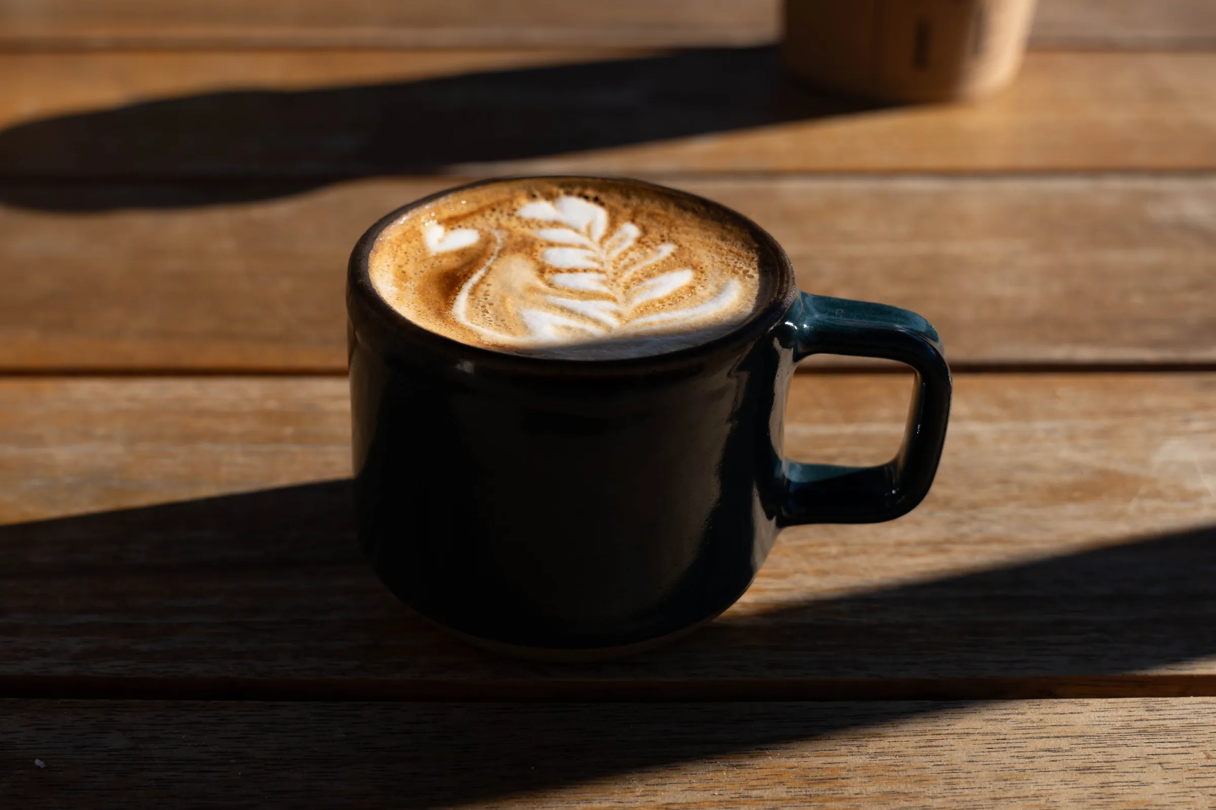 A flat white in a black cup on a wooden table, morning sun across the wood