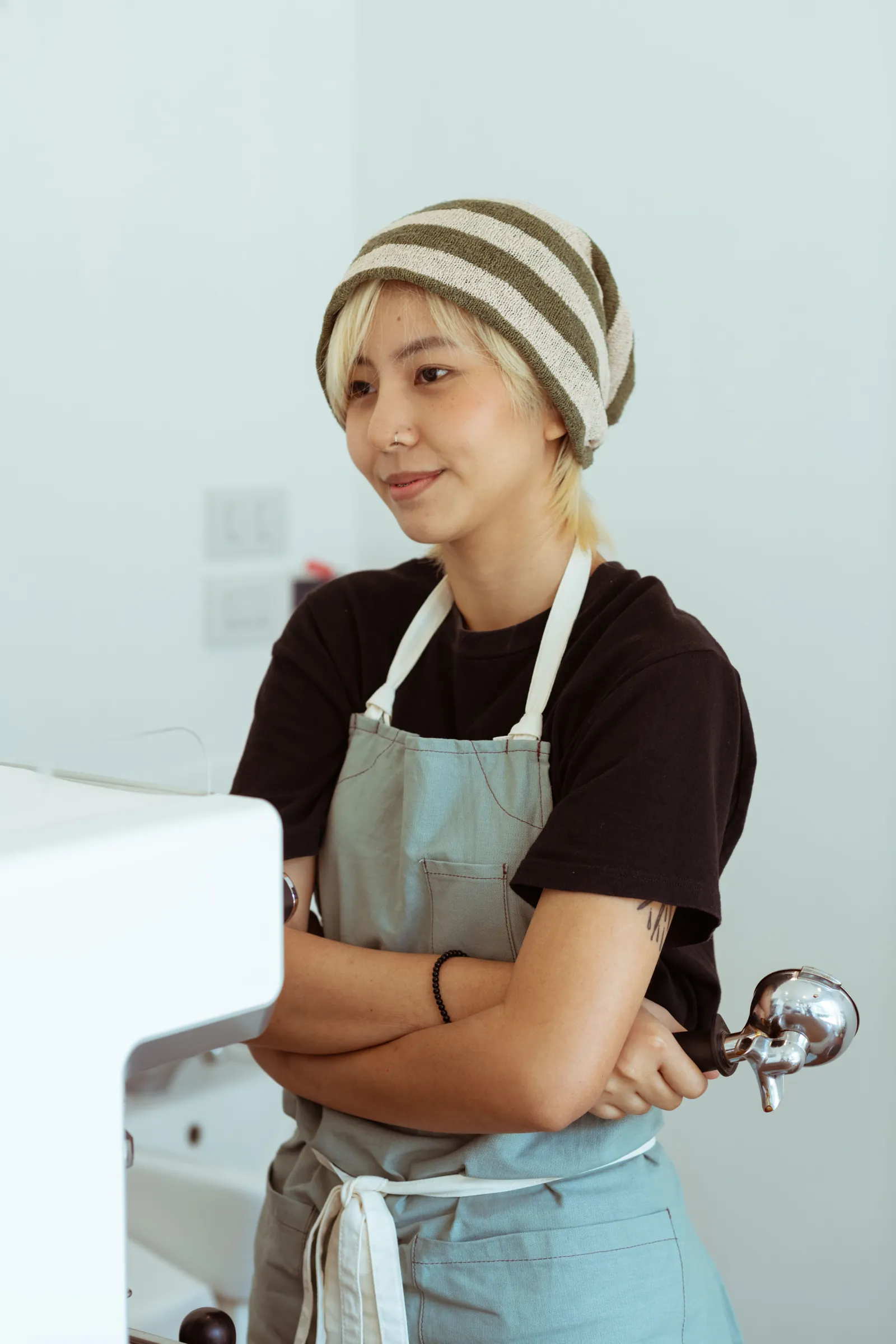 Ruth in a headscarf and apron, arms folded, in the kitchen