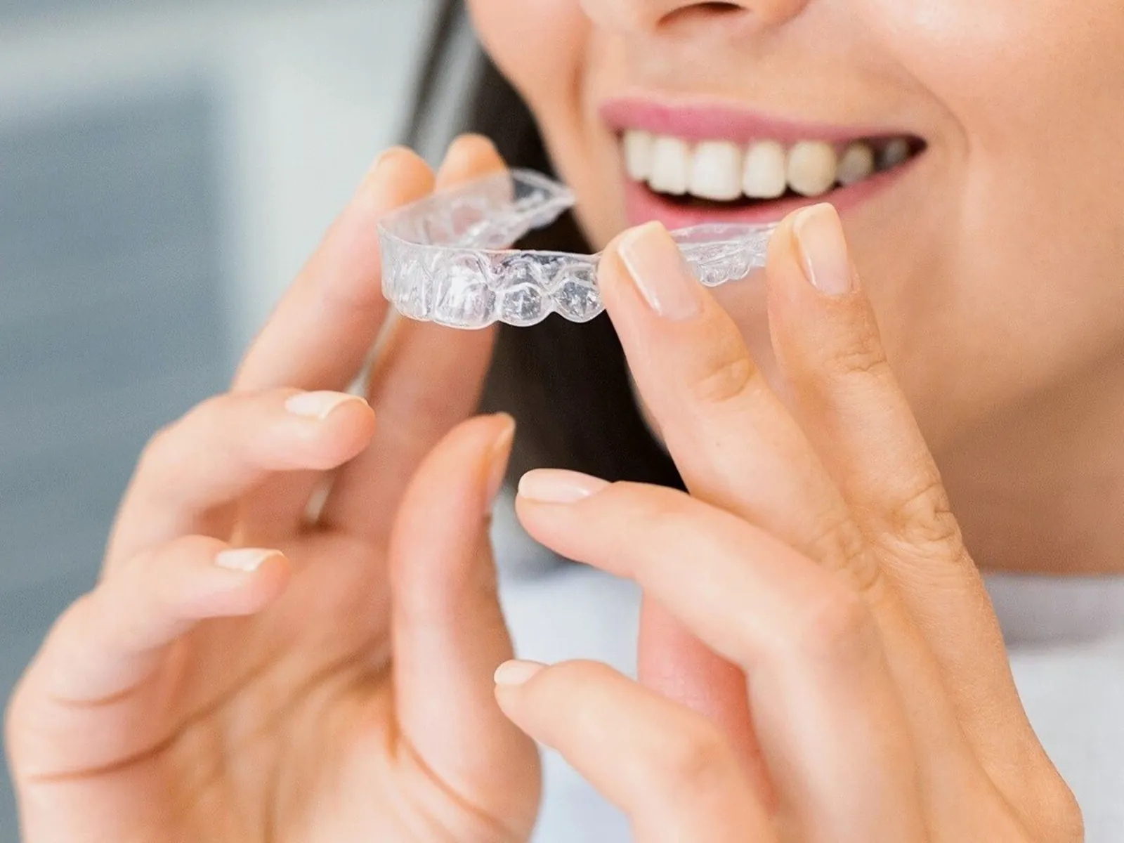 A woman fitting a clear aligner over her top teeth