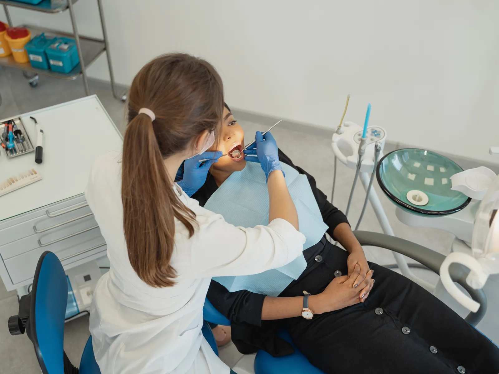 A dentist in a mask and cap leaning over a patient in a blue chair, examining their teeth