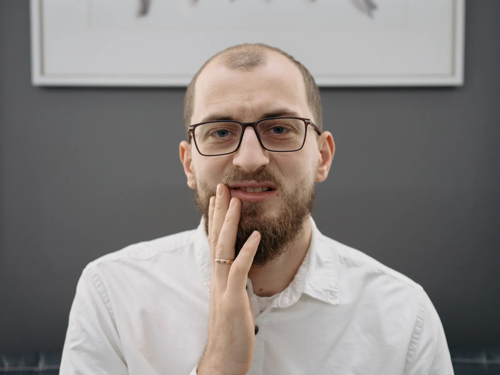 A man in glasses holding his jaw with a pained look