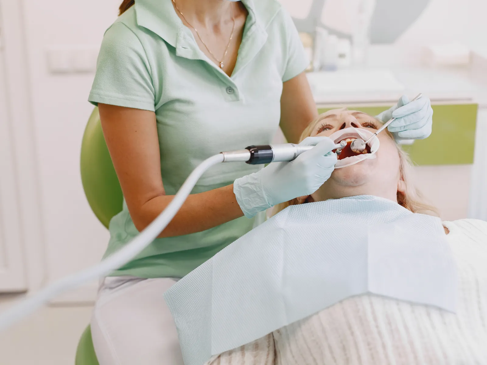A hygienist in green scrubs working on a patient wearing a paper bib
