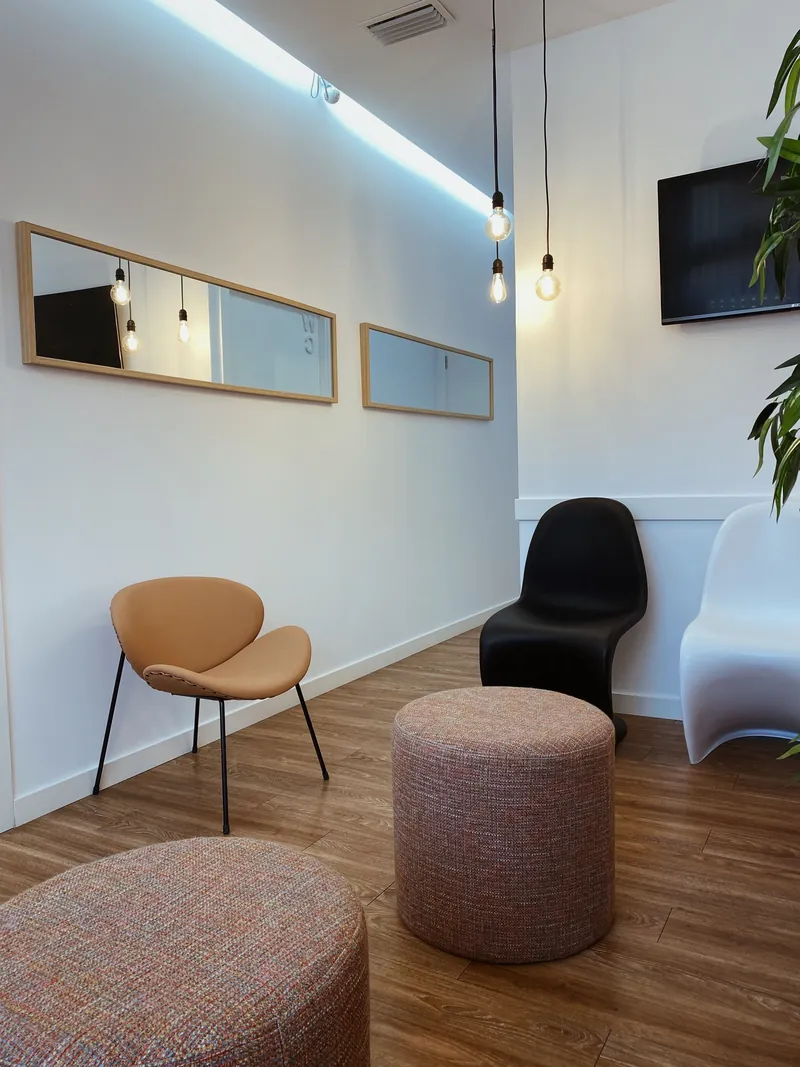 The waiting lounge: a tan chair, two stools and a plant by a mirror