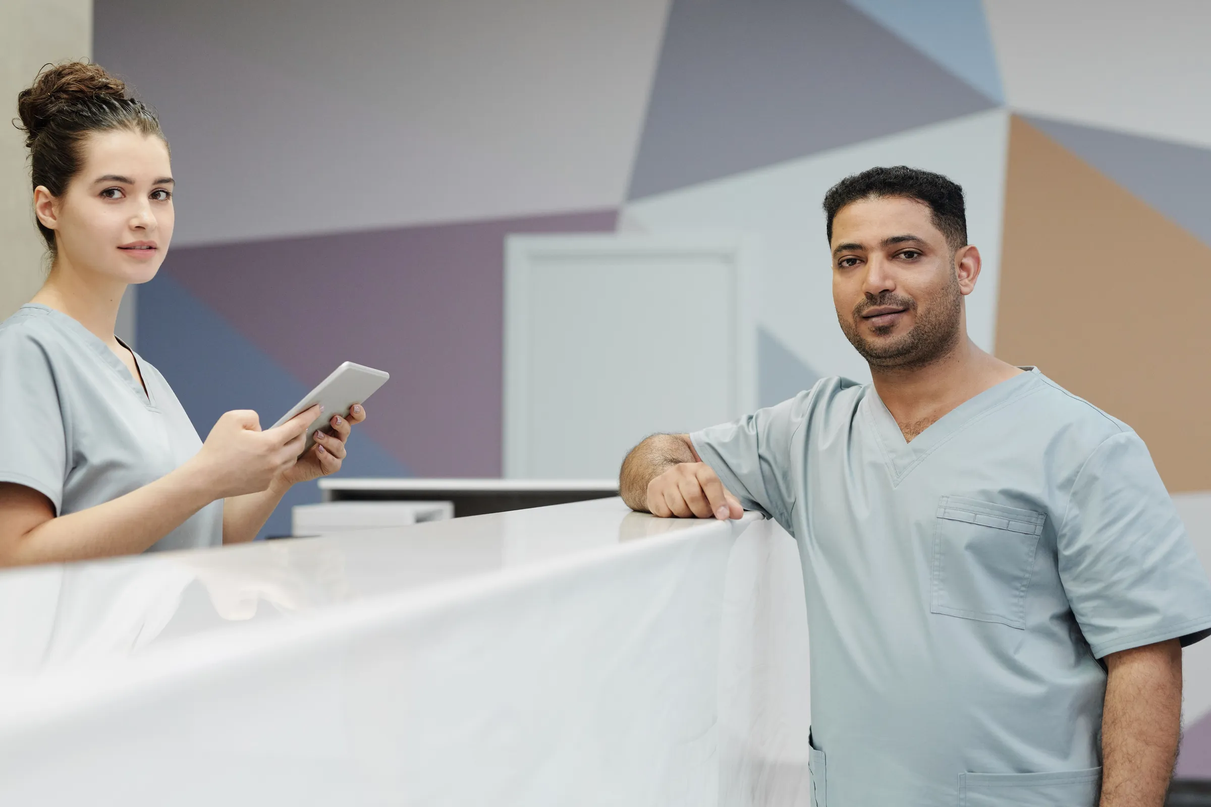 Two members of the team in grey scrubs at the reception desk, one holding a tablet