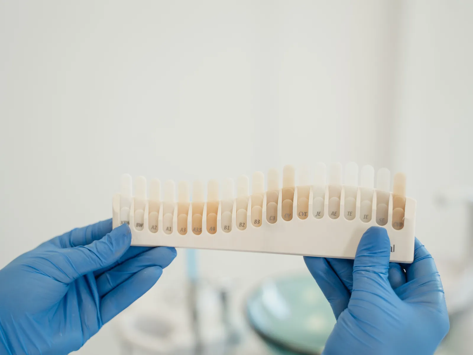 Gloved hands holding a row of tooth shade samples up against the light