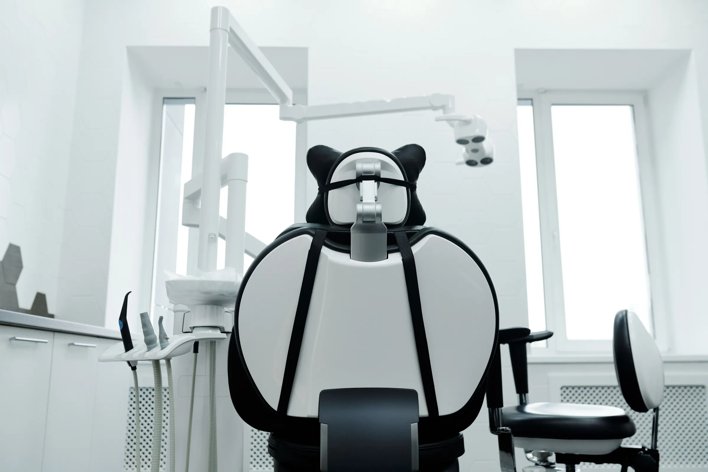 A white surgery with a black and white dental chair in front of two tall windows