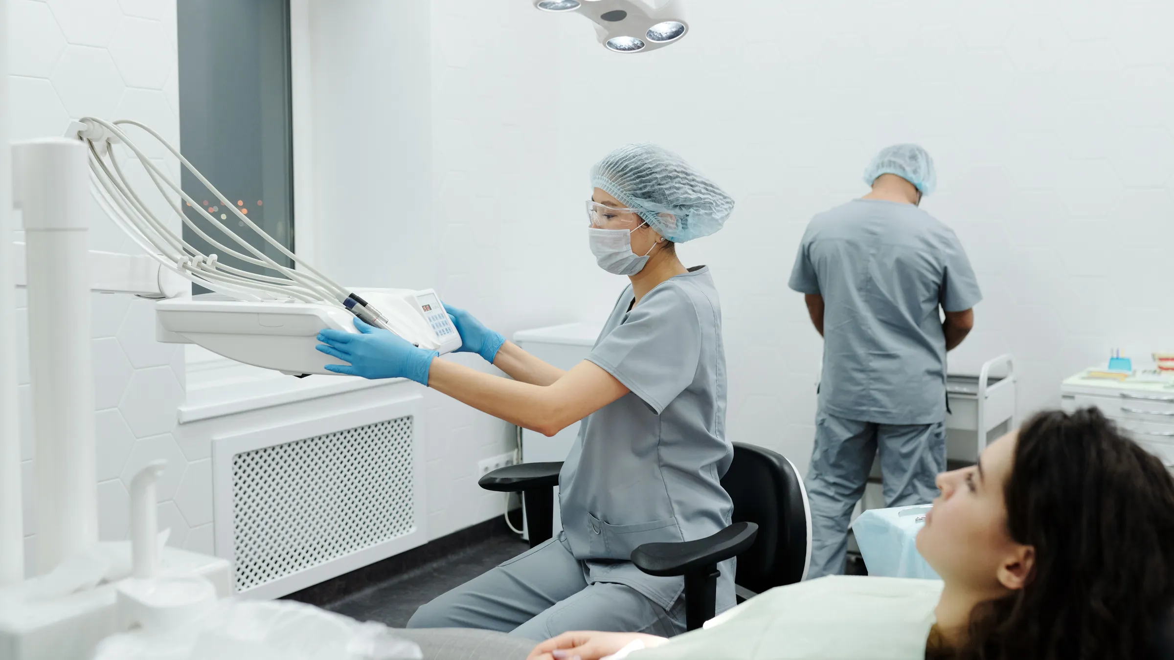 A surgery in use: a clinician in a hairnet and gloves reaching for an instrument while a patient lies in the chair