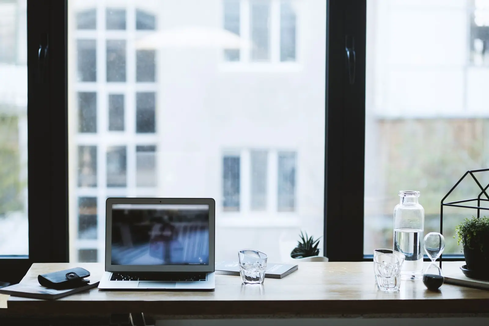 A desk and laptop set against a full-height window, with white-framed sash windows on the building opposite.