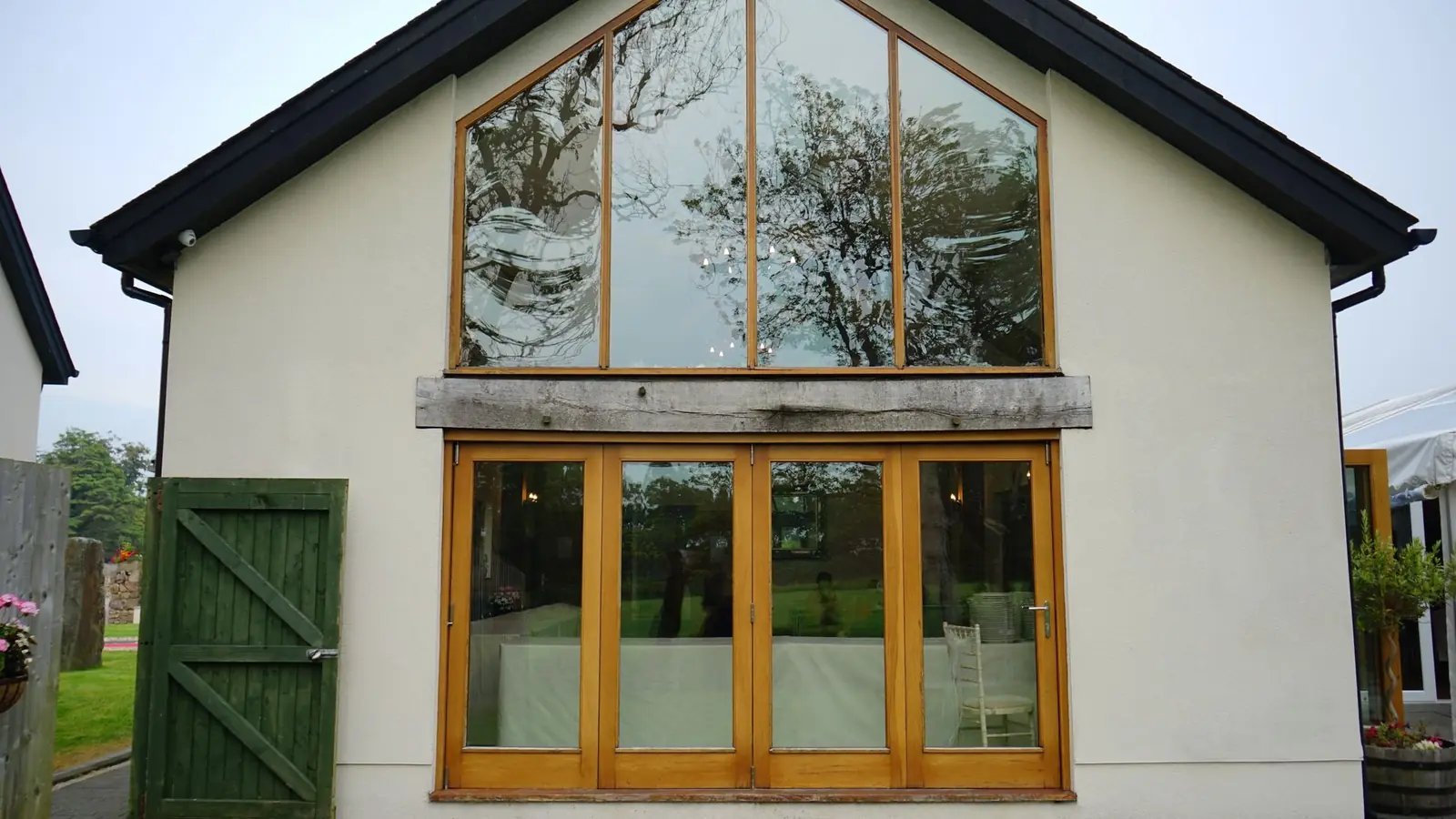 A rendered building with a tall oak-framed window and green timber doors.