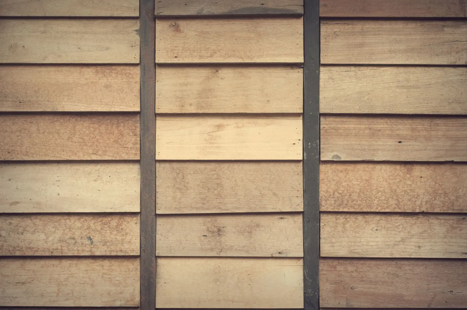 Horizontal timber cladding boards fixed to a frame, the grain lifting where the sun has caught it.