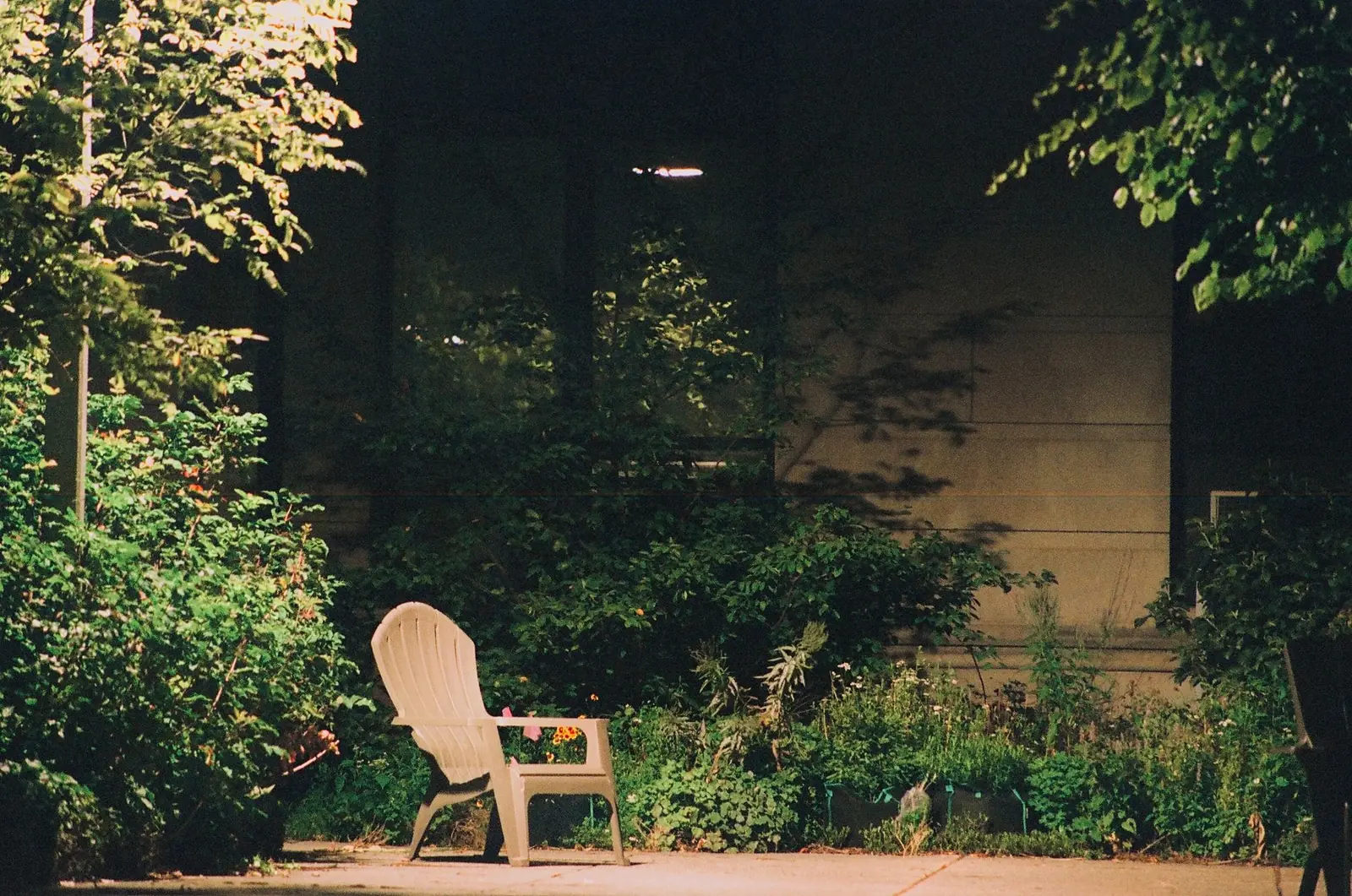 A quiet garden at dusk, a single chair on a path and a wall lit from below.