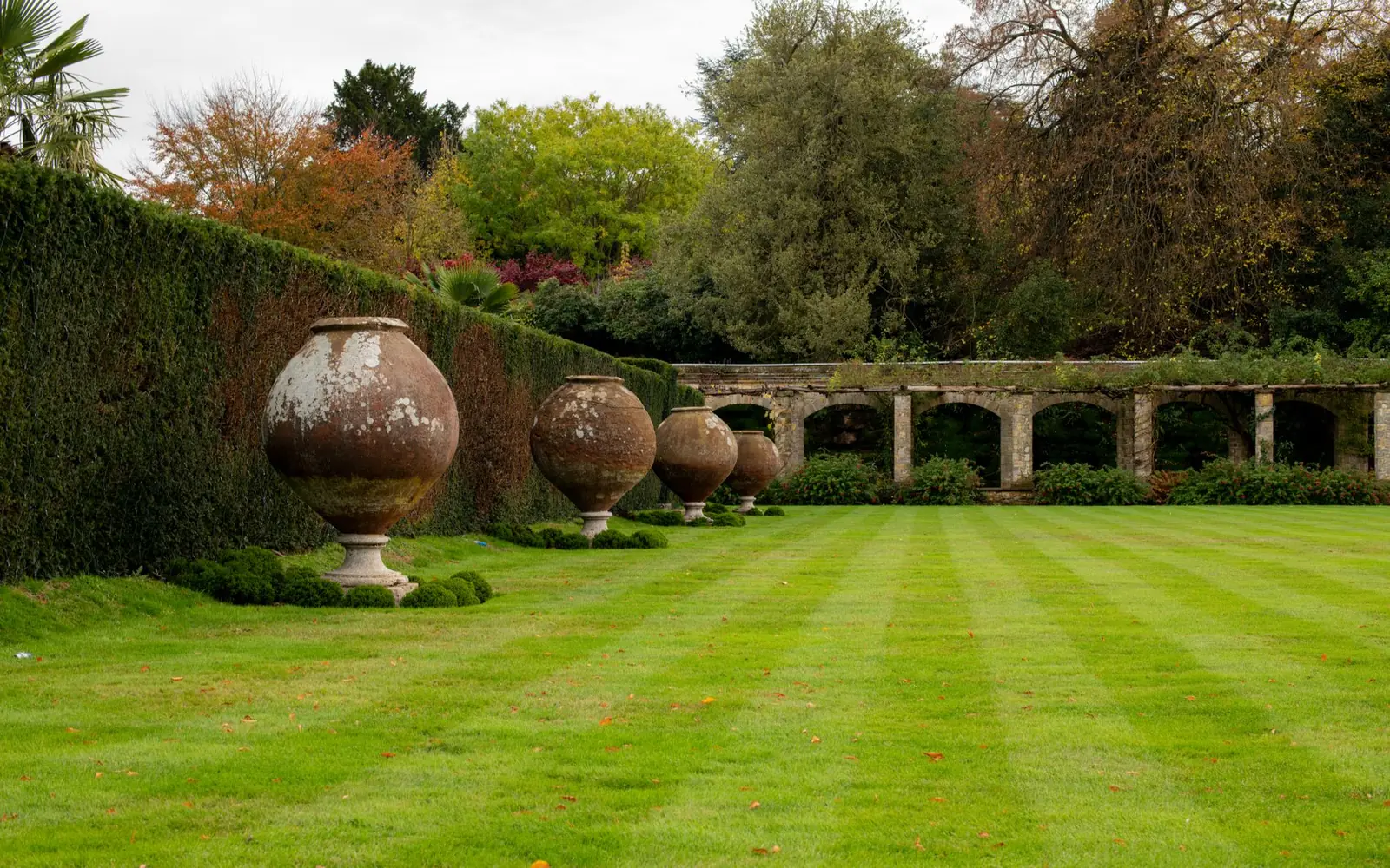 A striped lawn running to a stone arcade wall, with large planted urns along one edge.
