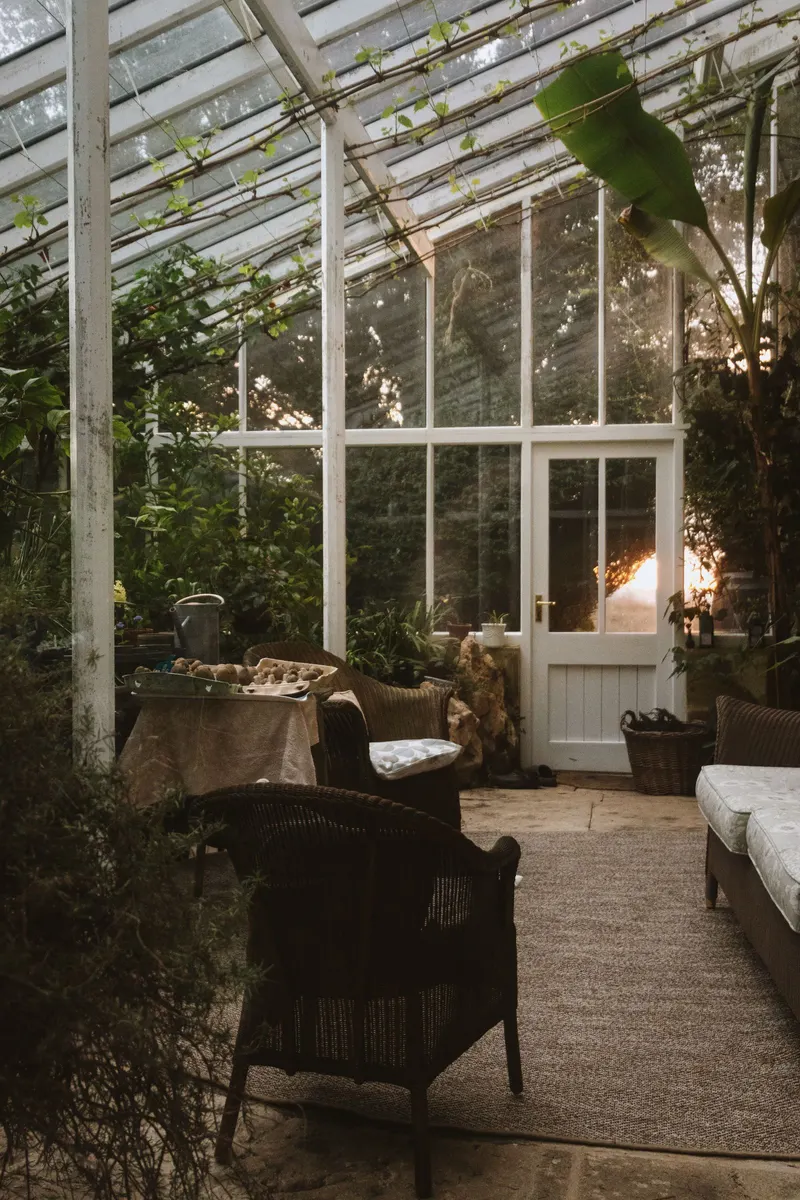 A Victorian conservatory with wicker chairs and a table, light coming through the glass roof.