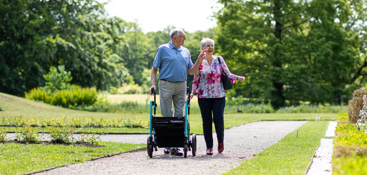 A couple walking a level garden path together, one of them with a wheeled walking frame.