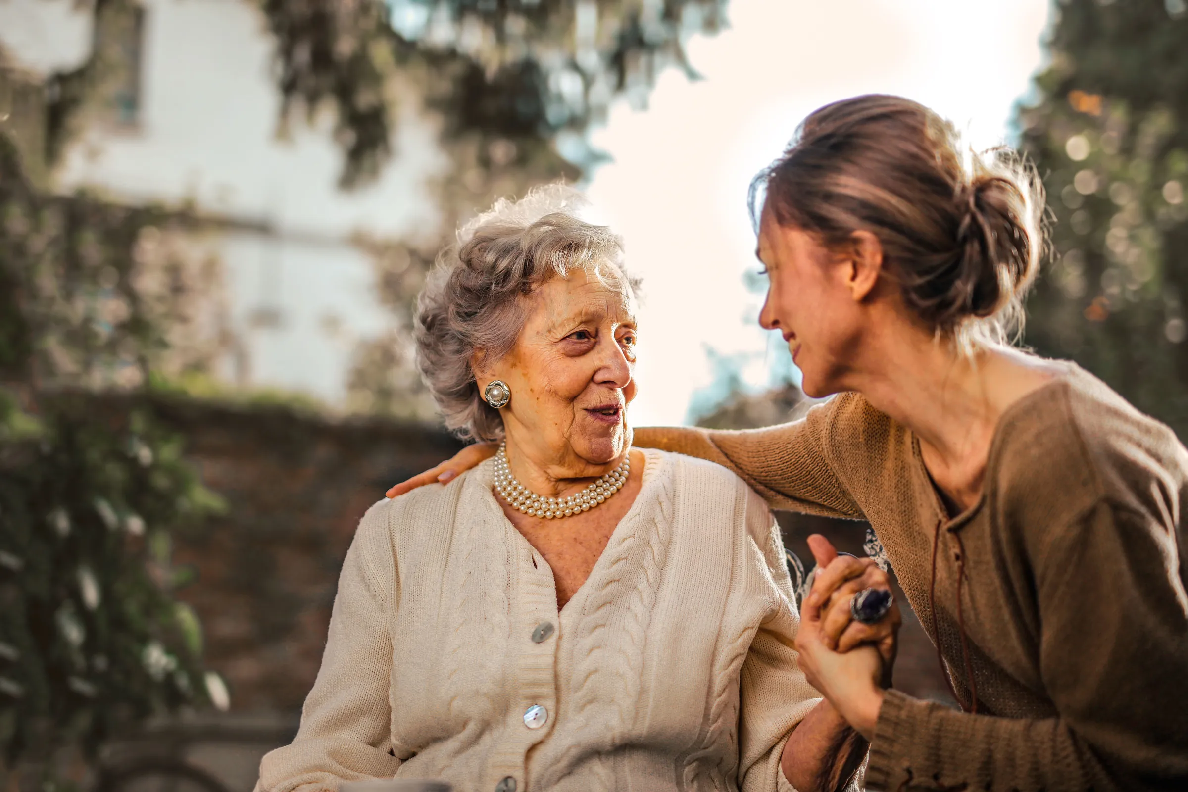 A carer and a resident laughing together on a garden bench in autumn sunlight.