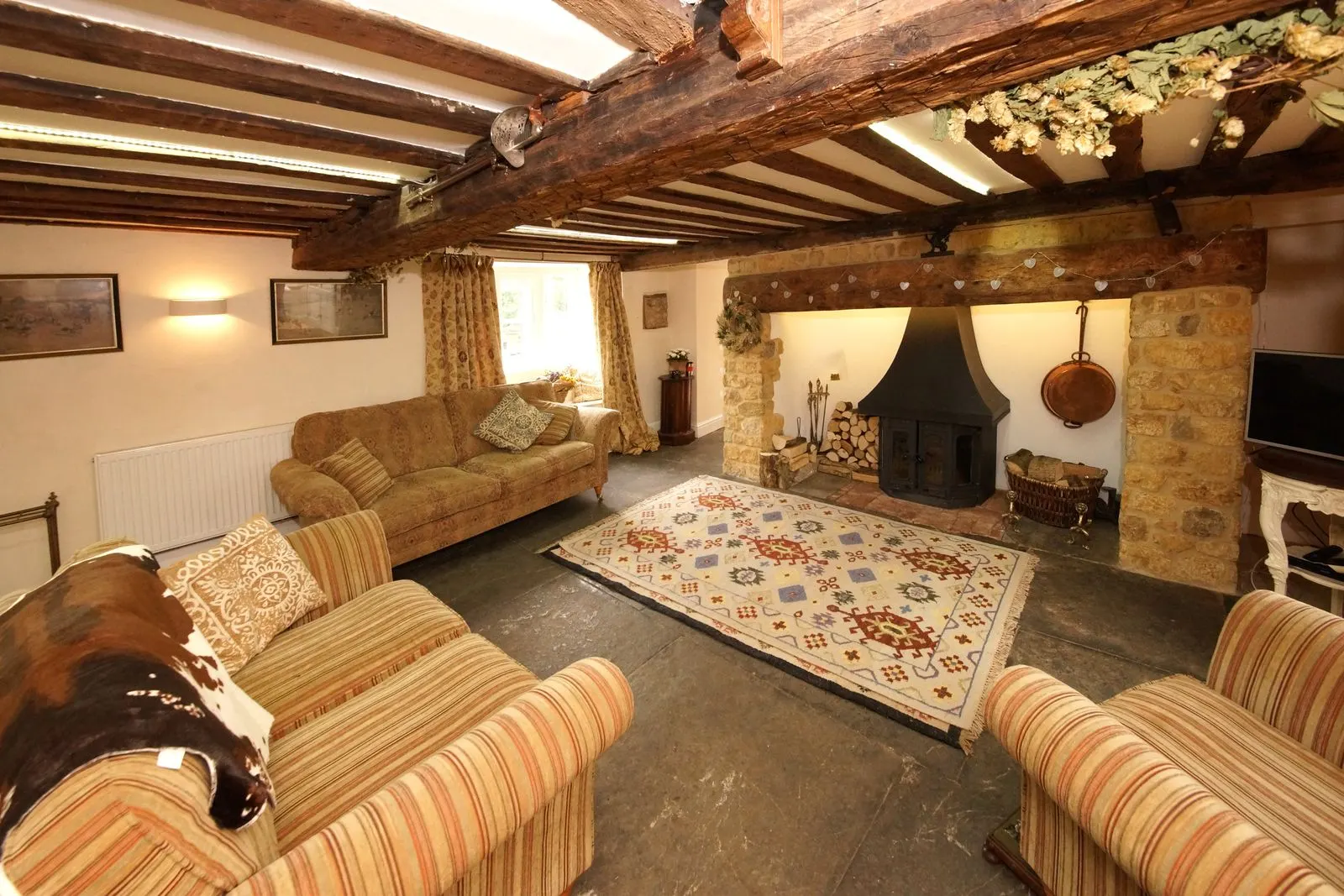 A beamed sitting room with striped sofas, a patterned rug and a stone fireplace.