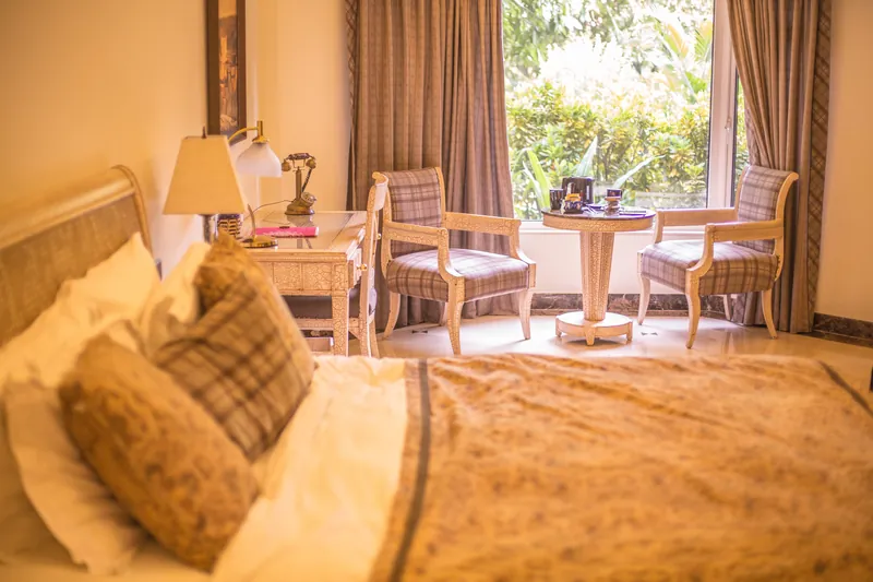 A sunlit bedroom with a bed, a small table and two chairs by a window onto the garden.