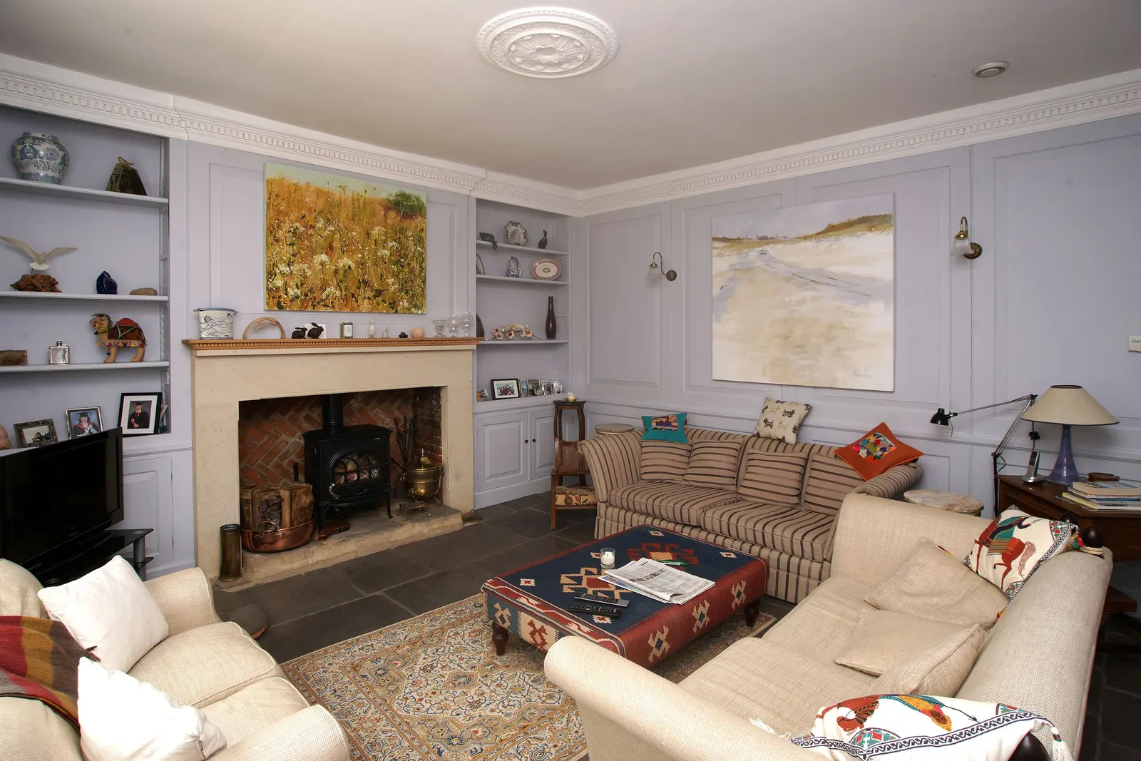 A sitting room with cream sofas, a stone fireplace and family photographs on the alcove shelves.