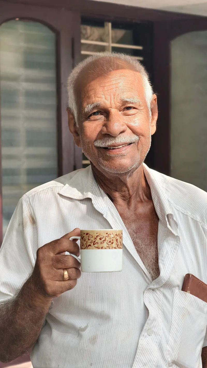 A resident smiling with a cup of tea by the conservatory door.